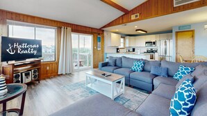 A spacious living room with a large grey sofa, a coffee table, and a television on a wooden stand. - Attitude Adjustment: Dog-friendly, ocean/sound views, shared pool (Avon)