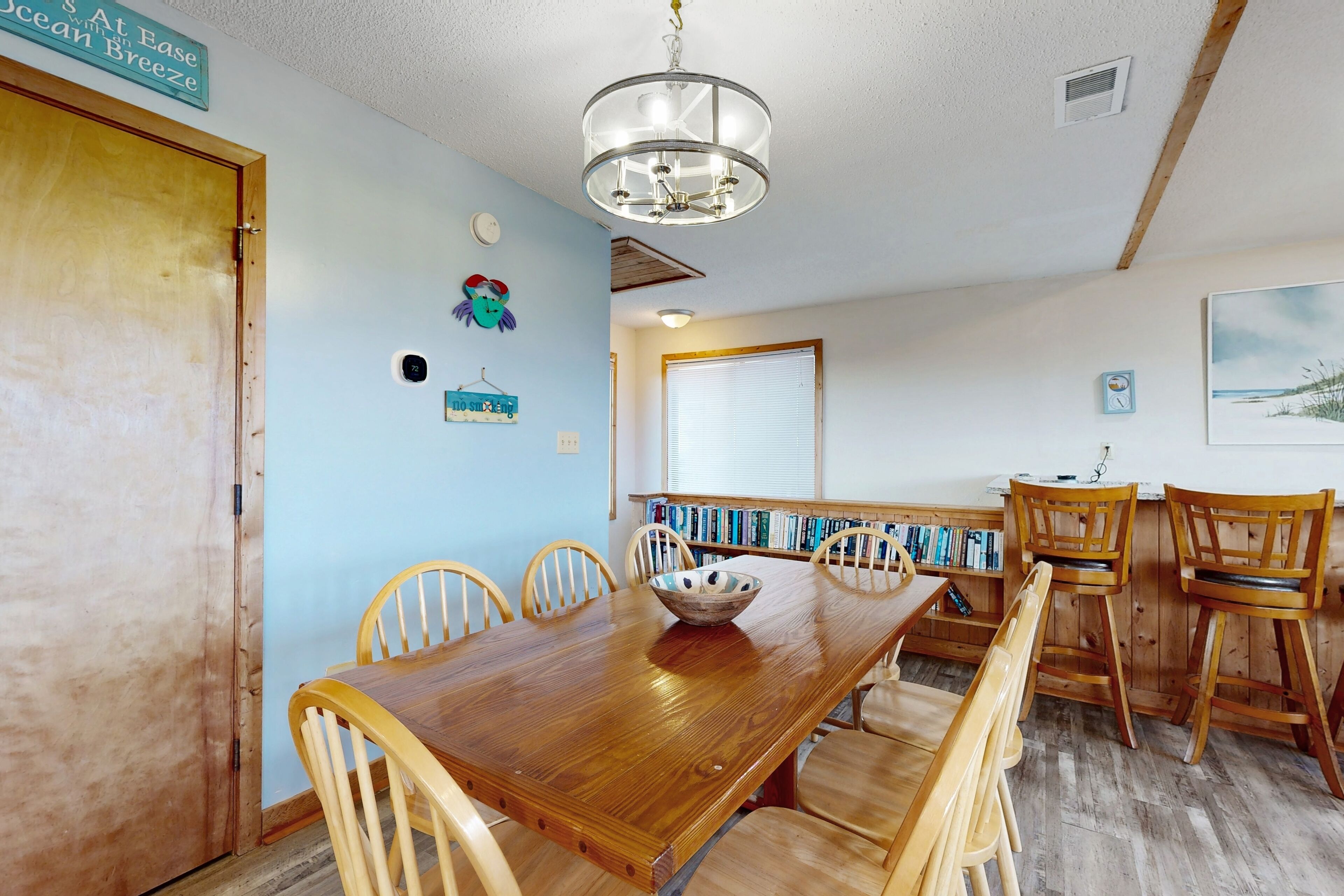A dining area with a wooden table and chairs, a chandelier, and a bookshelf with books.