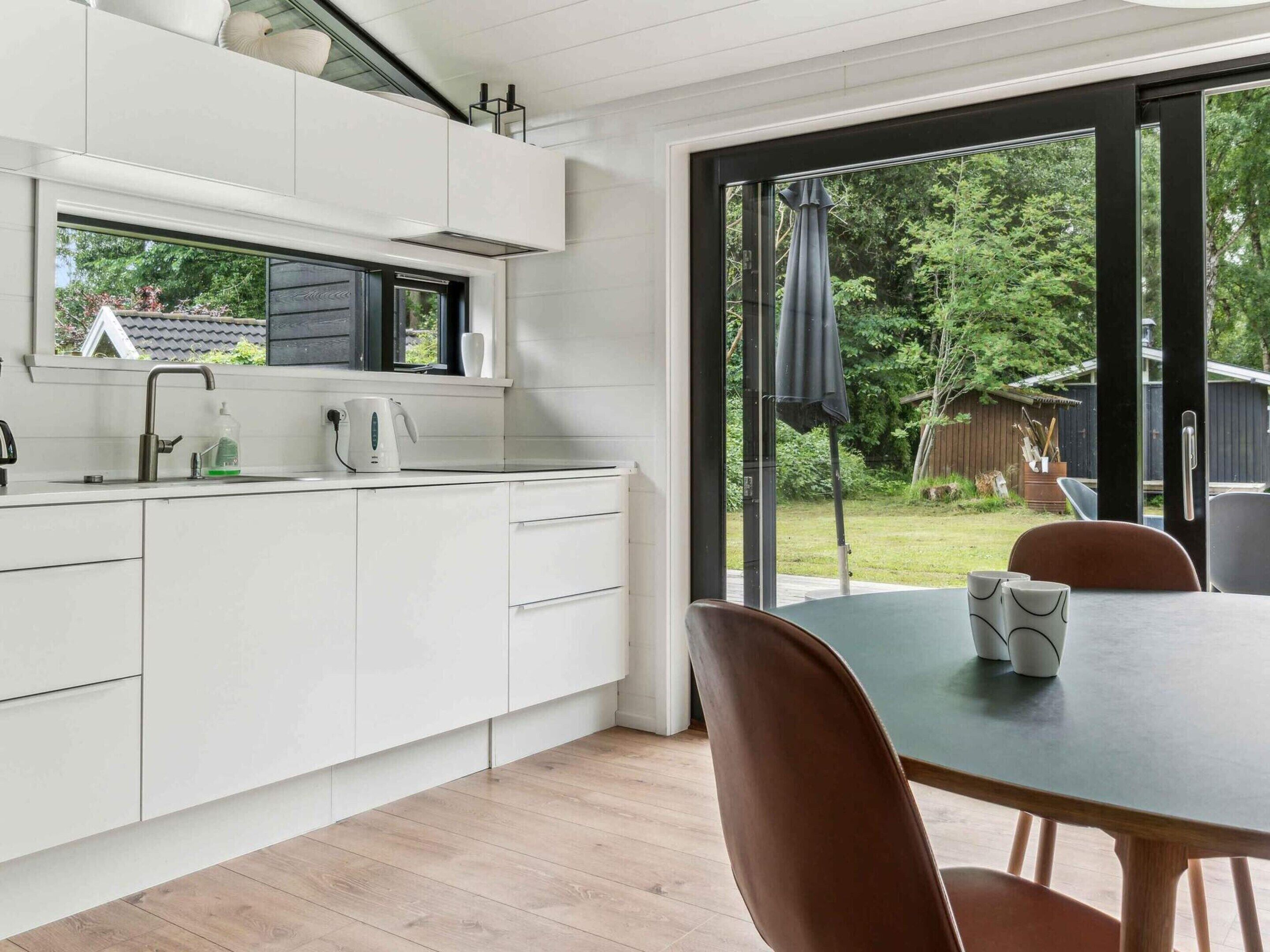 A modern kitchen with white cabinets, a window, and a dining area with a table and chairs.