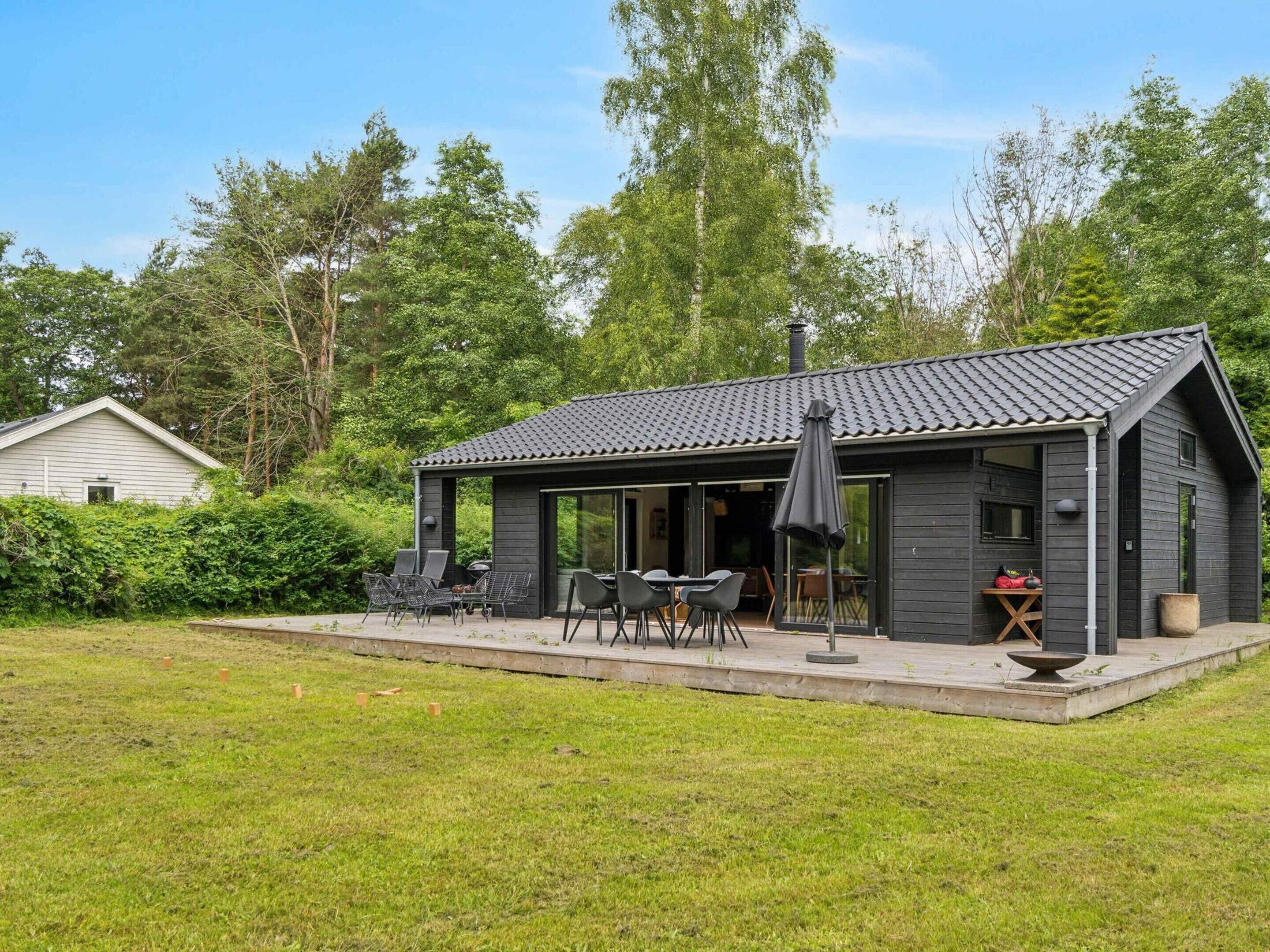 Eine moderne Holzhütte mit überdachter Terrasse, Sitzgelegenheiten im Freien und einem großen Fenster.