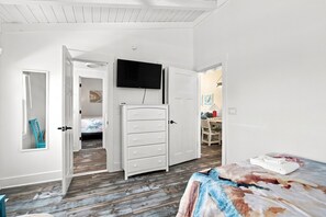 Une chambre à coucher comprenant un lit, une commode, un téléviseur et une porte donnant sur une autre pièce.