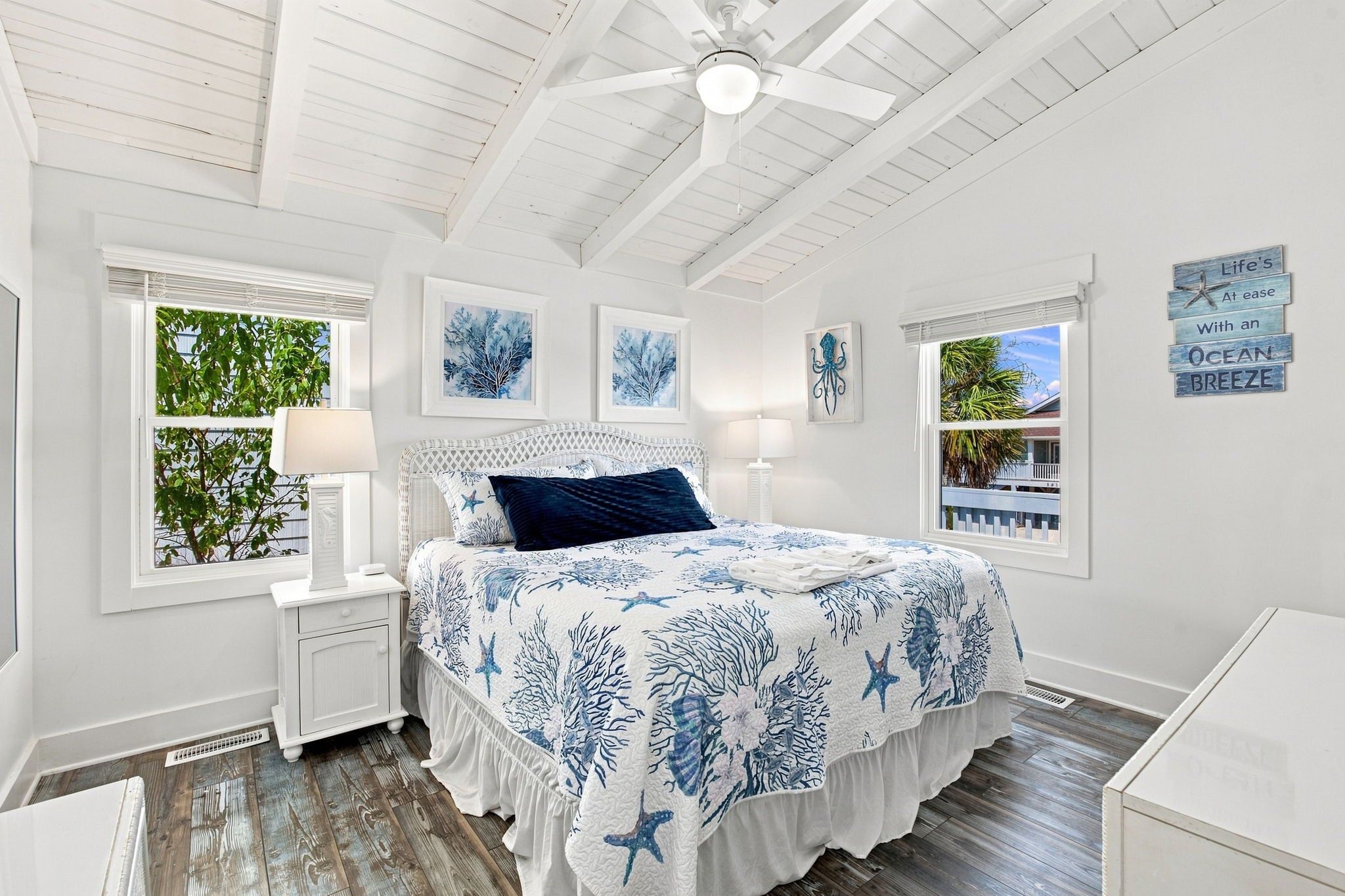 Une chambre à coucher avec un lit, des tables de chevet, un ventilateur de plafond et des œuvres d’art accrochées aux murs.