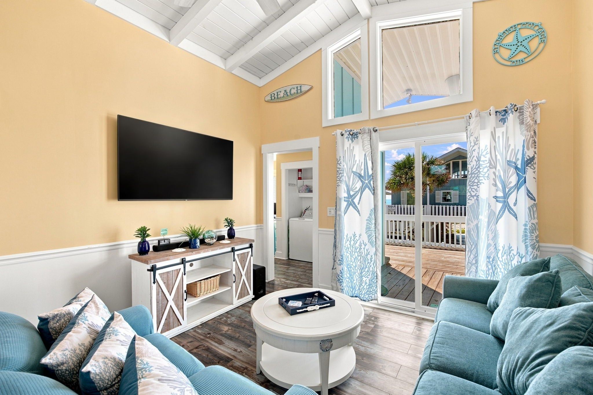 Una sala de estar con televisor, sofá, mesa de centro y vistas al exterior.