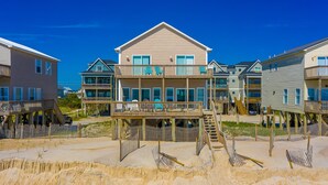 Ein Strandgrundstück mit mehreren Gebäuden, darunter ein auffälliges zweistöckiges Haus mit Balkon sowie ein kleinerer Anbau.