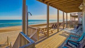Eine Holzterrasse mit Picknicktischen und Liegestühlen mit Blick auf einen Strand.
