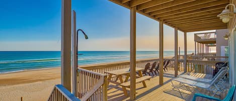 A wooden deck with picnic tables and lounge chairs overlooking a beach.