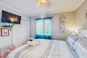 Une chambre à coucher comprenant un lit, un téléviseur, une fenêtre avec des rideaux, un climatiseur fixé au mur et un tableau.