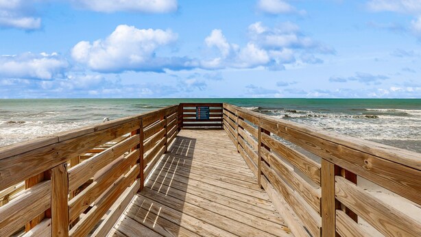 Una passerella di legno che conduce alla spiaggia, con vista libera sull'oceano e sul cielo.