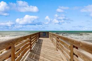 Une promenade en bois menant à la plage, offrant une vue dégagée sur l’océan et le ciel.