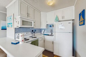 A compact kitchen with white cabinetry, a microwave, a stove, and a refrigerator.