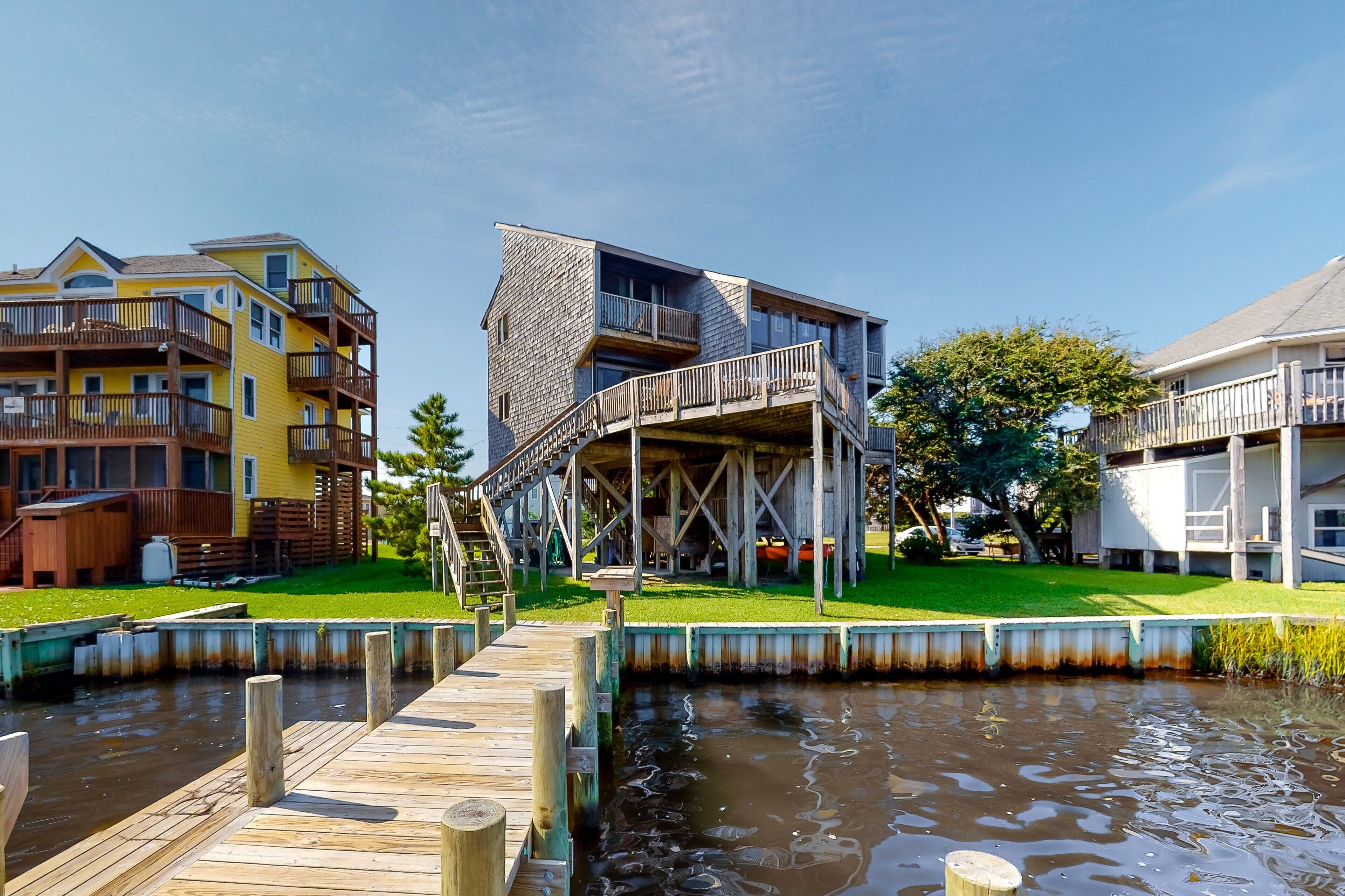Una propiedad frente al agua con un muelle que conduce a un edificio con terraza de madera y una escalera.