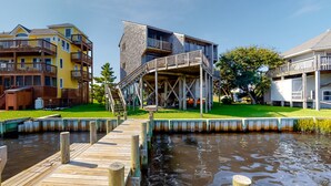 Una propiedad frente al agua con un muelle que conduce a un edificio con terraza de madera y una escalera.
