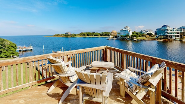 Una terraza de madera con dos sillas Adirondack mirando al agua.