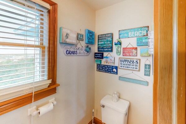 A bathroom with a toilet, a window with blinds, and various motivational signs on the wall.
