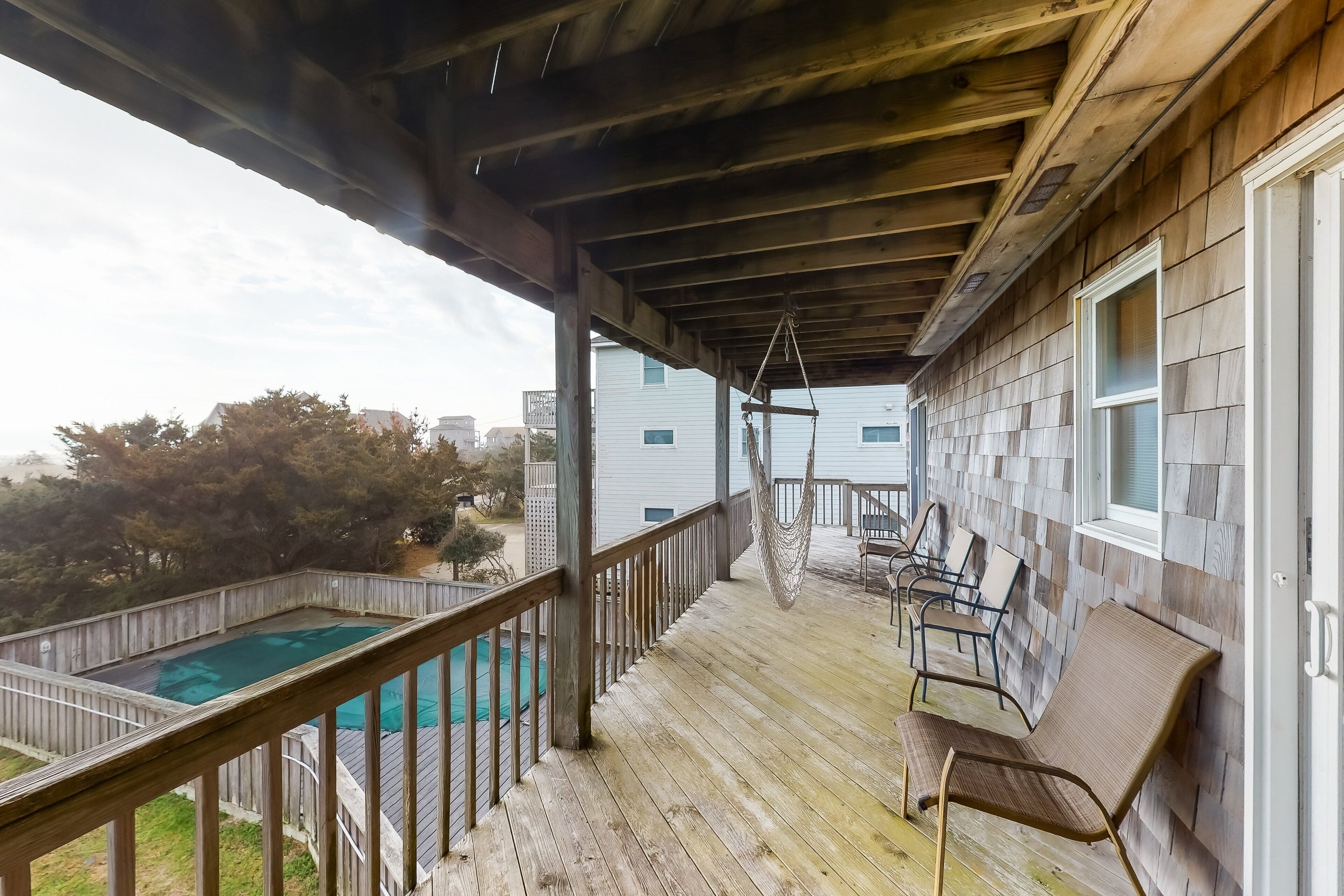 A wooden deck with a pool, chairs, and a hammock.