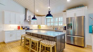 Une cuisine moderne avec des meubles blancs, un réfrigérateur en acier inoxydable, des tabourets de bar en bois et des luminaires suspendus.