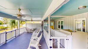 Une véranda couverte avec des balustrades blanches, un ventilateur de plafond et une rangée de chaises en plastique blanches.