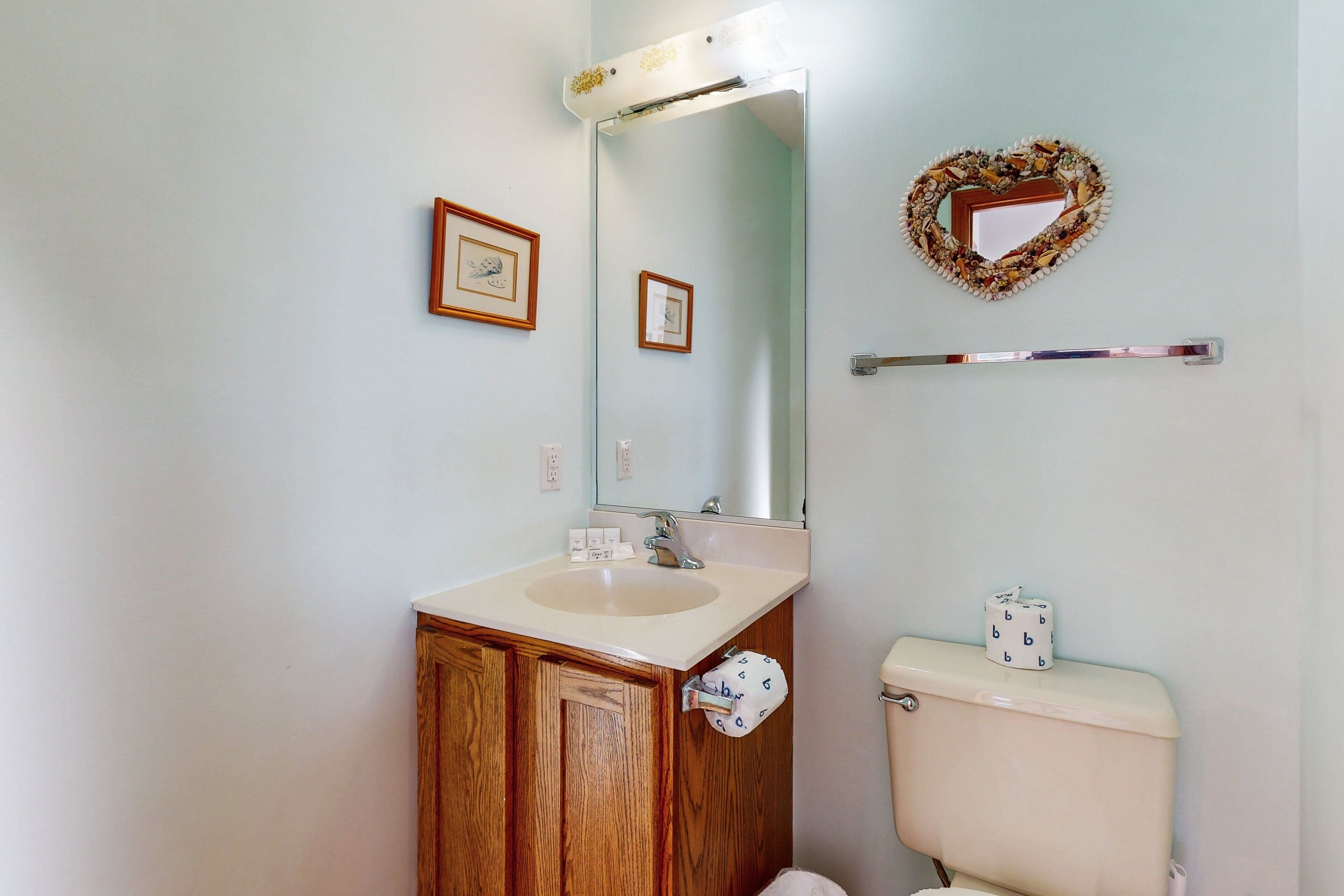 A bathroom with a wooden cabinet, a sink, a mirror, a toilet, and a decorative heart-shaped mirror frame.