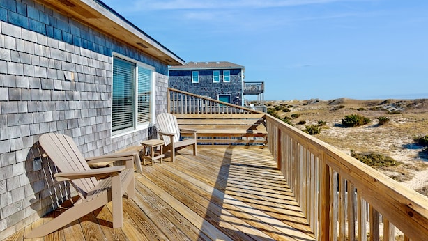 A wooden deck with Adirondack chairs, a wooden railing, and a view of a house with a blue exterior and a window with shutters. - Oceanfront house w/private hot tub, balcony, washer/dryer, WiFi, central AC (Waves)