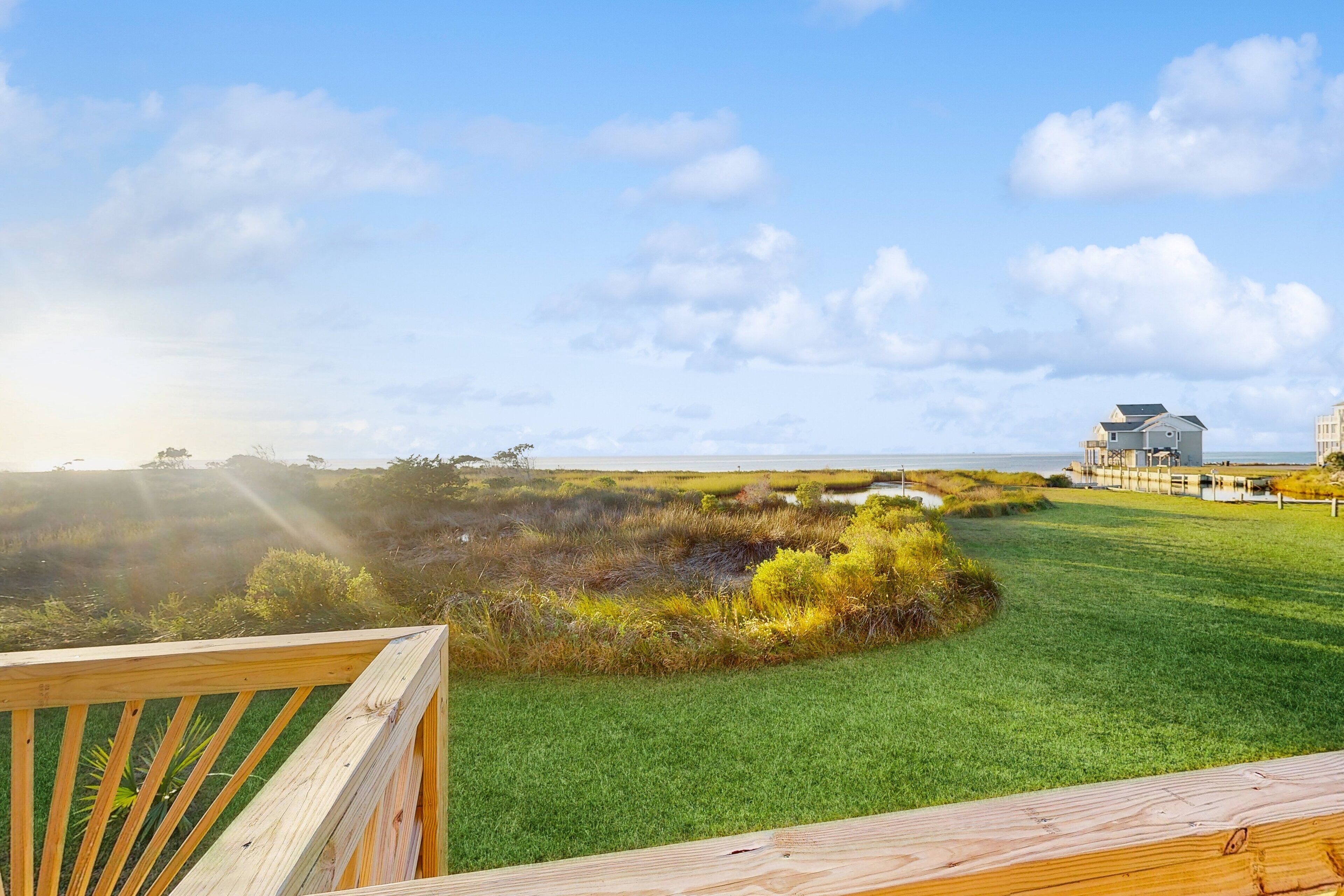 Una terraza de madera con vistas a un área verde y al océano, con un edificio a lo lejos.