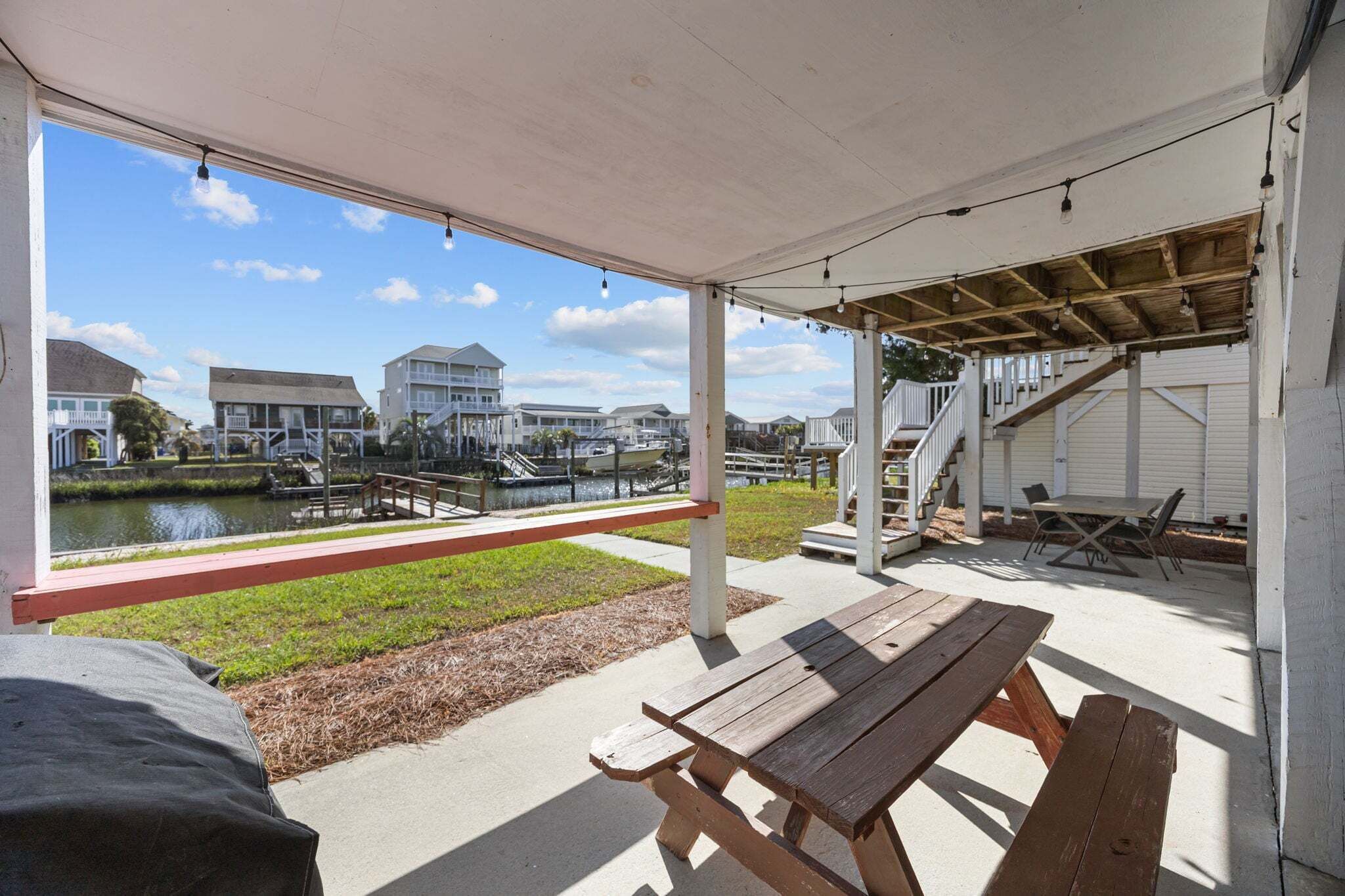 A covered patio with picnic tables, a view of a water body, and a staircase leading to a building.