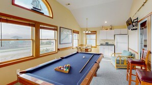A pool table with a view of the outdoors, a dining area, and a kitchen.