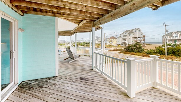 A wooden deck with a white railing, a door, and a view of houses and beach in the background.
