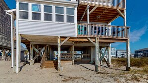 A two-story wooden structure with a balcony, a staircase, and a sandy ground. - Summer Sands: Waterfront, Dog Friendly, Balcony (Ocean Isle Beach)