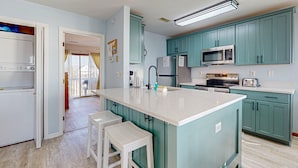 A kitchen with teal cabinets, a white countertop, and a central island with stools. - Summer Sands: Waterfront, Dog Friendly, Balcony (Ocean Isle Beach)