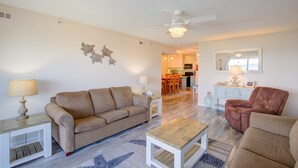 A living room with a beige sofa, a wooden coffee table, a red armchair, and a ceiling fan. - Oceanfront condo with elevator, private beach, ocean view, community pool, grill (North Topsail Beach)