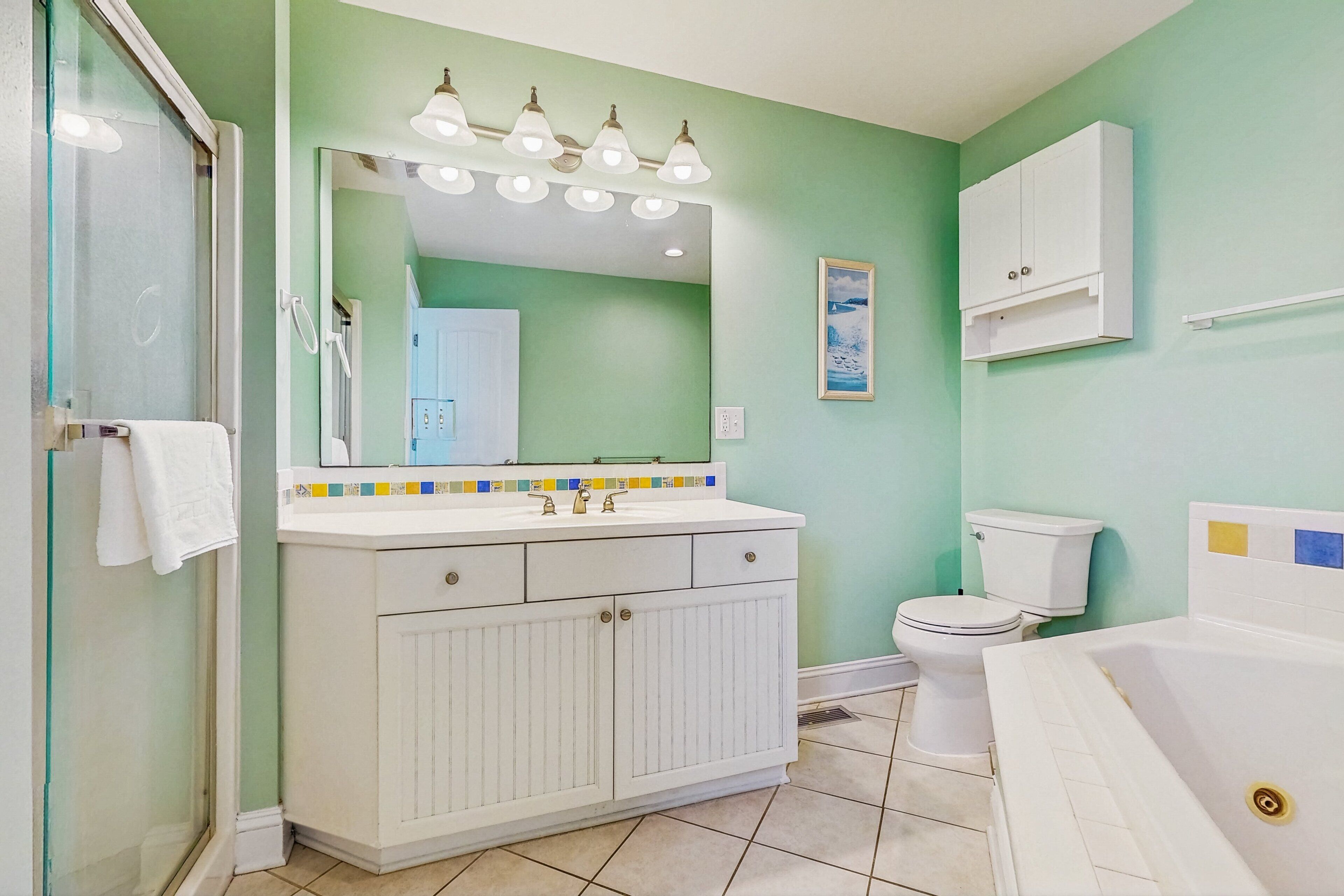 Une salle de bain avec une douche à parois de verre, un lavabo blanc avec un pare-éclaboussures carrelé, un grand miroir et une baignoire blanche.