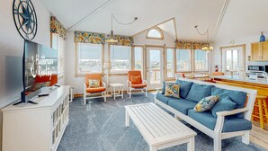 Un grand espace de vie comprenant un canapé, une table basse et des fauteuils, un téléviseur, ainsi qu’un coin cuisine avec un comptoir et des placards.