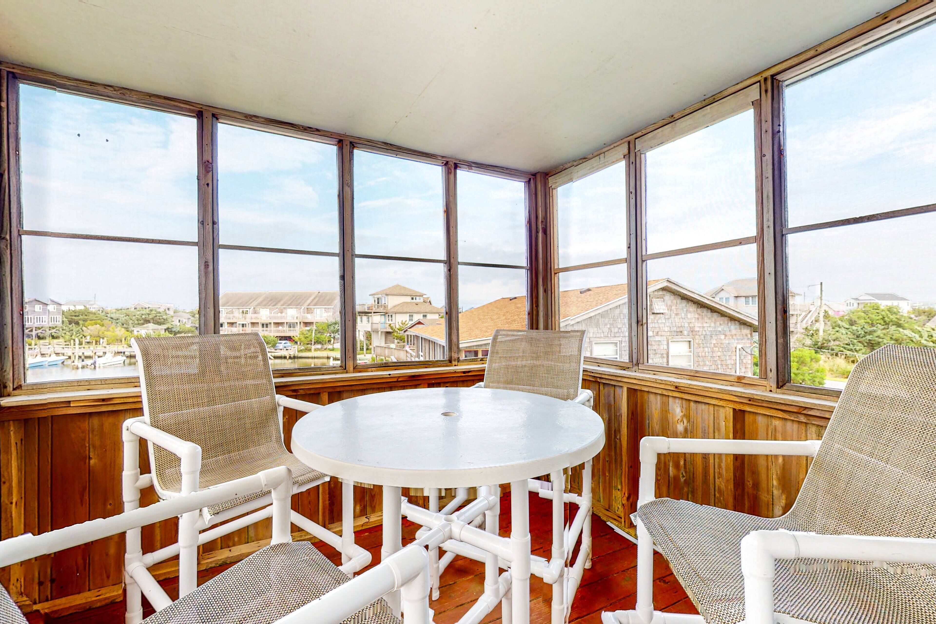 A sunroom with a round table and four chairs, large windows, and a view of buildings and a body of water.