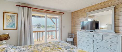 A bedroom with a bed, a dresser, a television, and a balcony with a view.