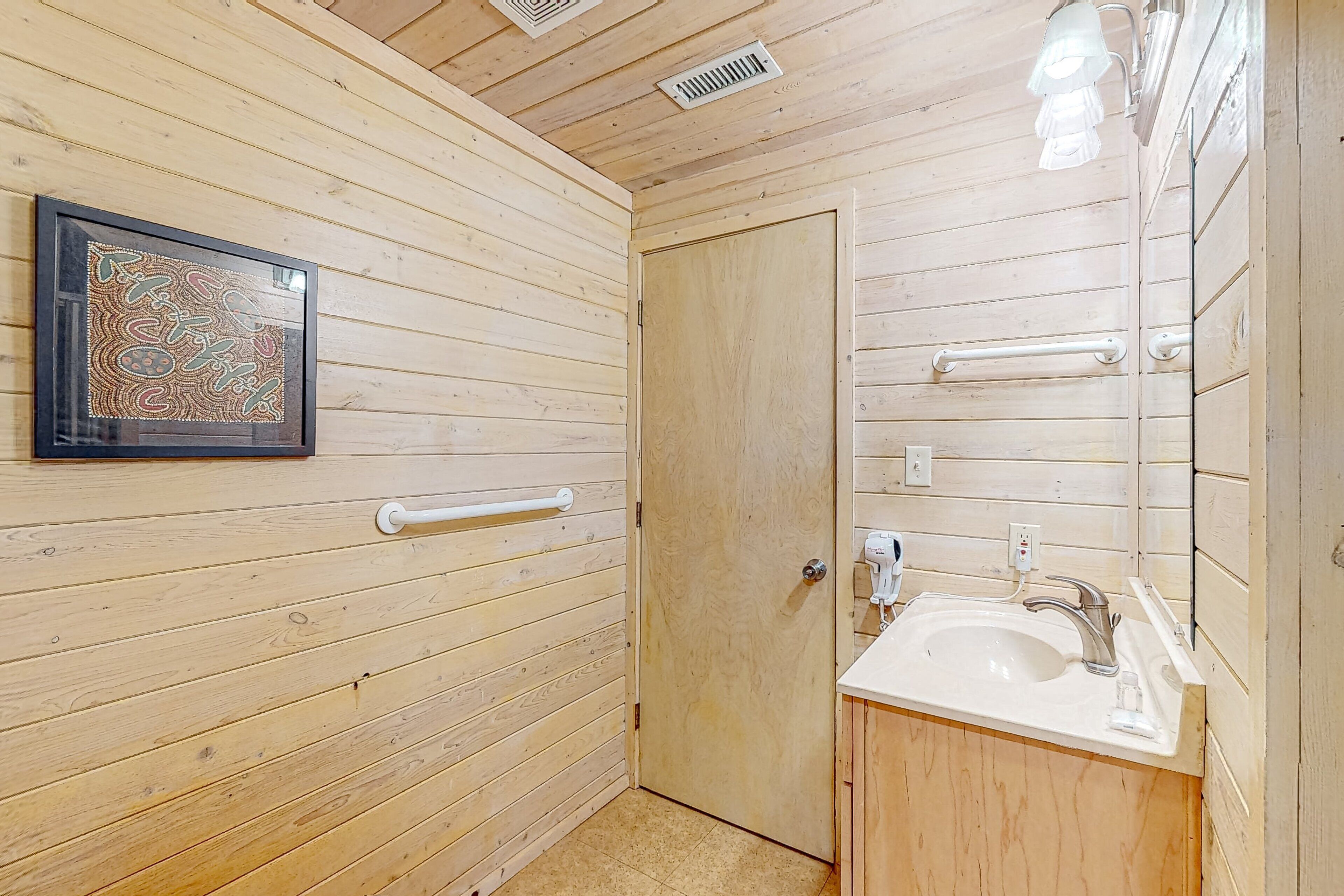 A wooden-paneled bathroom with a sink, mirror, and handrails.