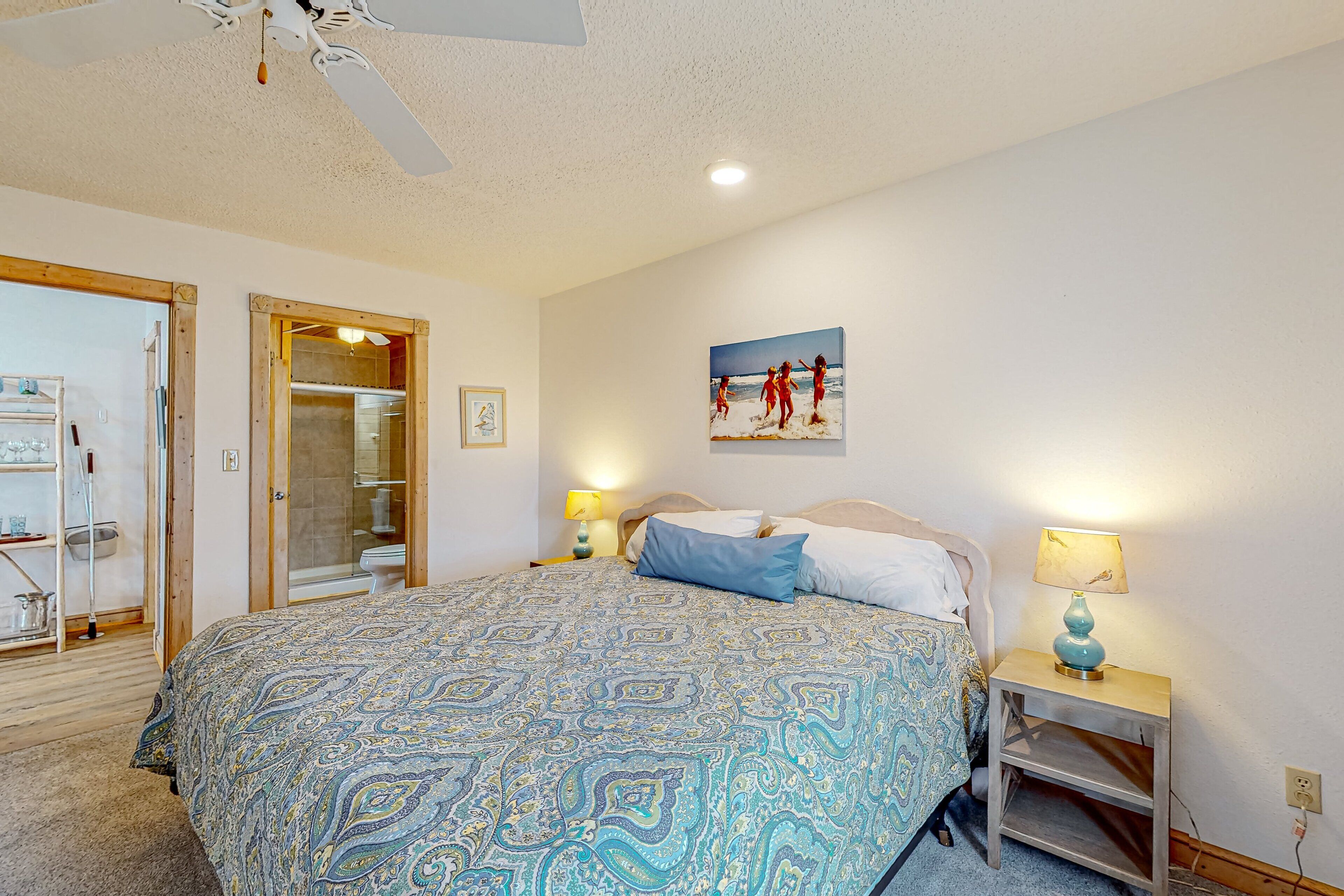 A bedroom with a patterned bedspread, a painting on the wall, and a bedside table with a lamp.