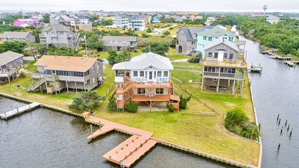 Une propriété située au bord de l’eau, dotée d’un quai, d’une grande maison avec balcon et d’un bâtiment plus petit avec une terrasse.