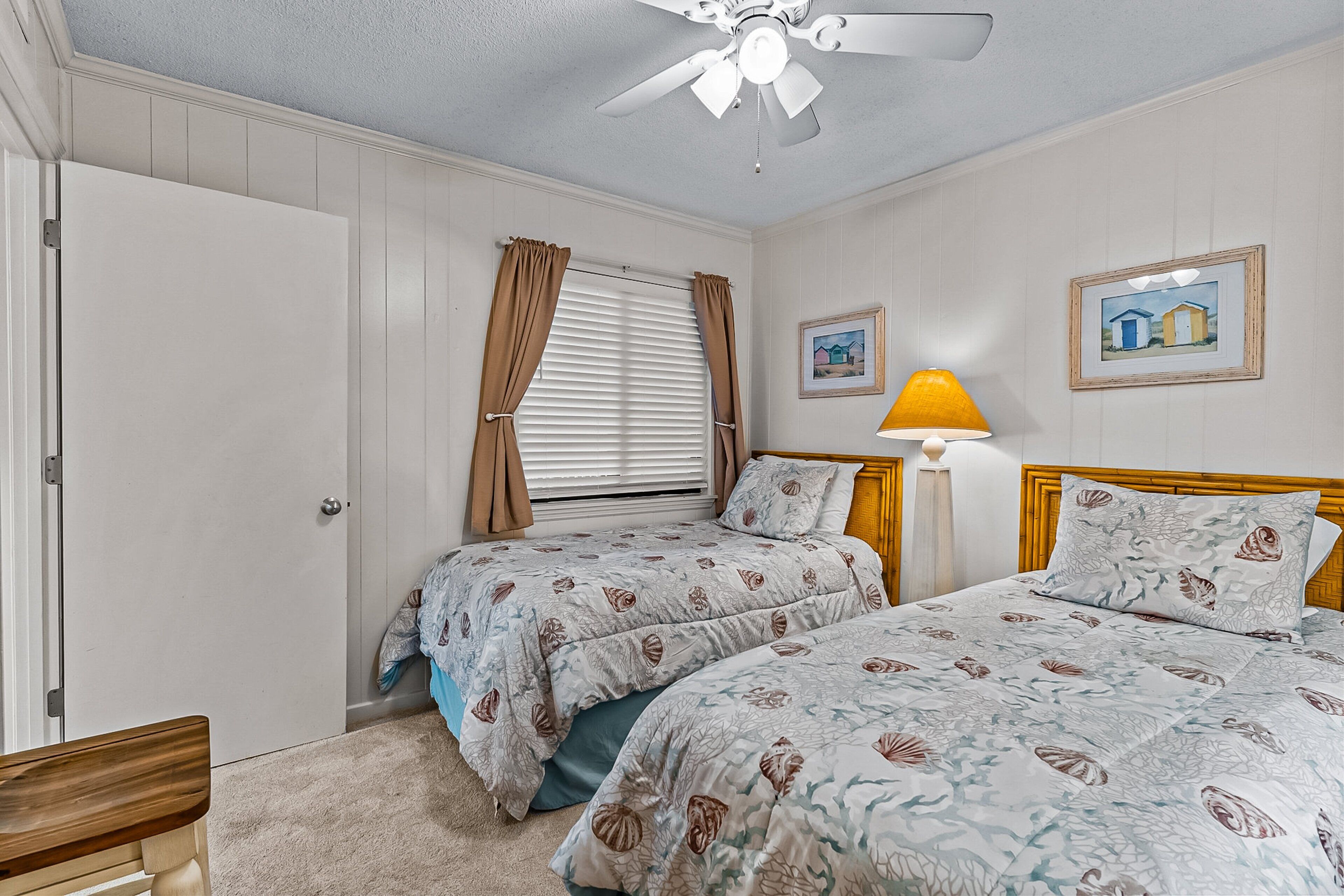 A bedroom with two beds, a ceiling fan, a nightstand, and a lamp.