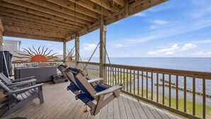A wooden deck with a swing chair, a hot tub, and a view of the water.