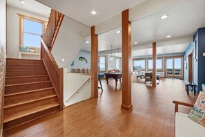 A spacious room with a wooden staircase, a pool table, and large windows offering a view.