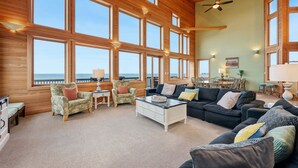 A spacious living room with large windows, a ceiling fan, and a view of the ocean.