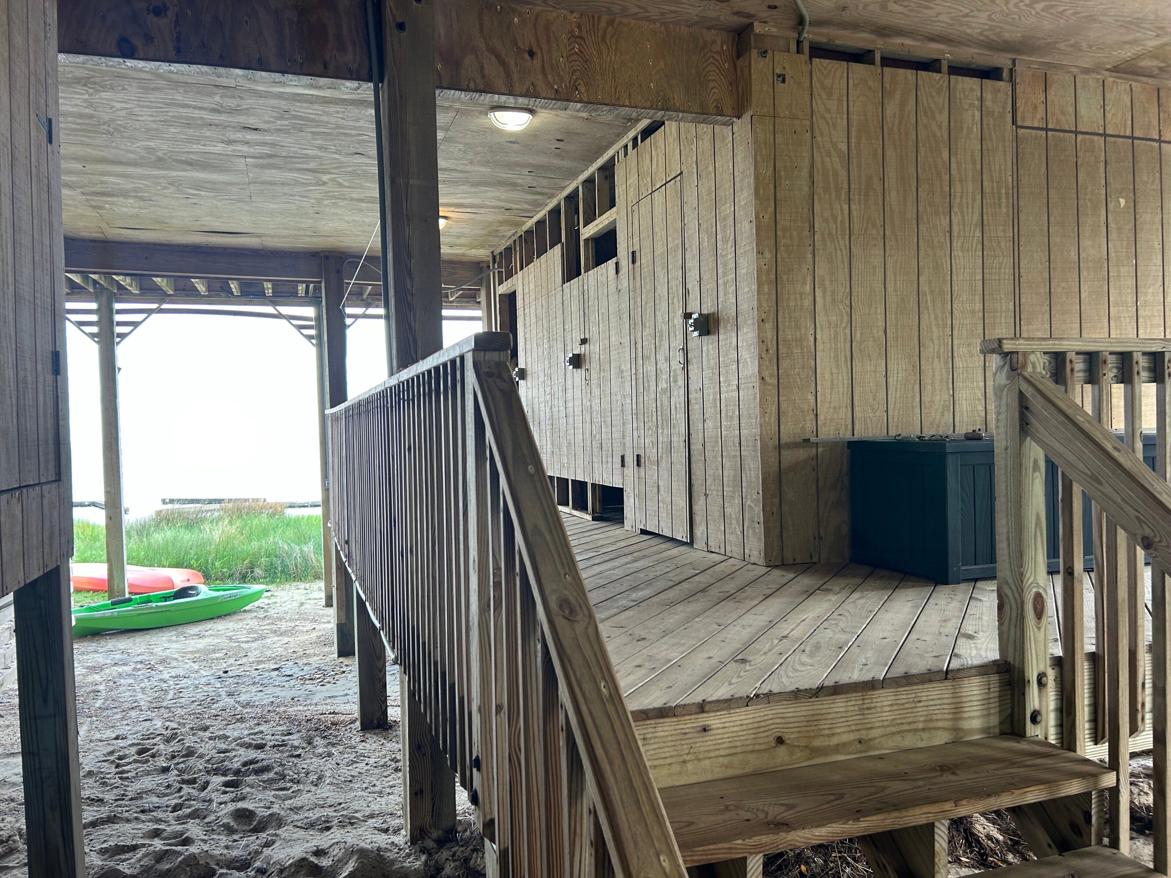 Eine Holzterrasse mit Geländer, ein überdachter Bereich mit einer Bank und ein Kajak im Hintergrund.