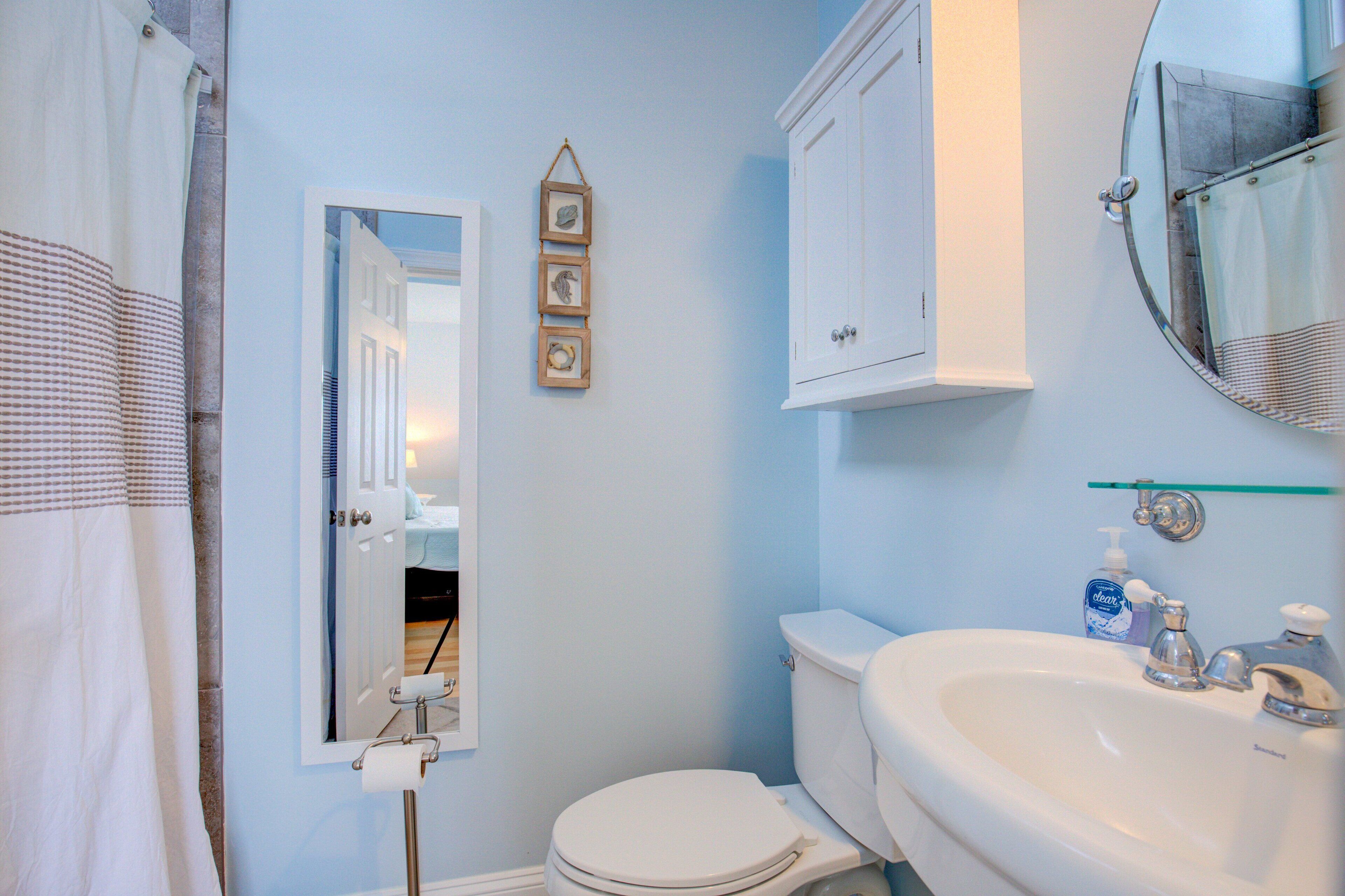 A bathroom with a toilet, sink, and mirror. There is a shower curtain and a framed picture on the wall.