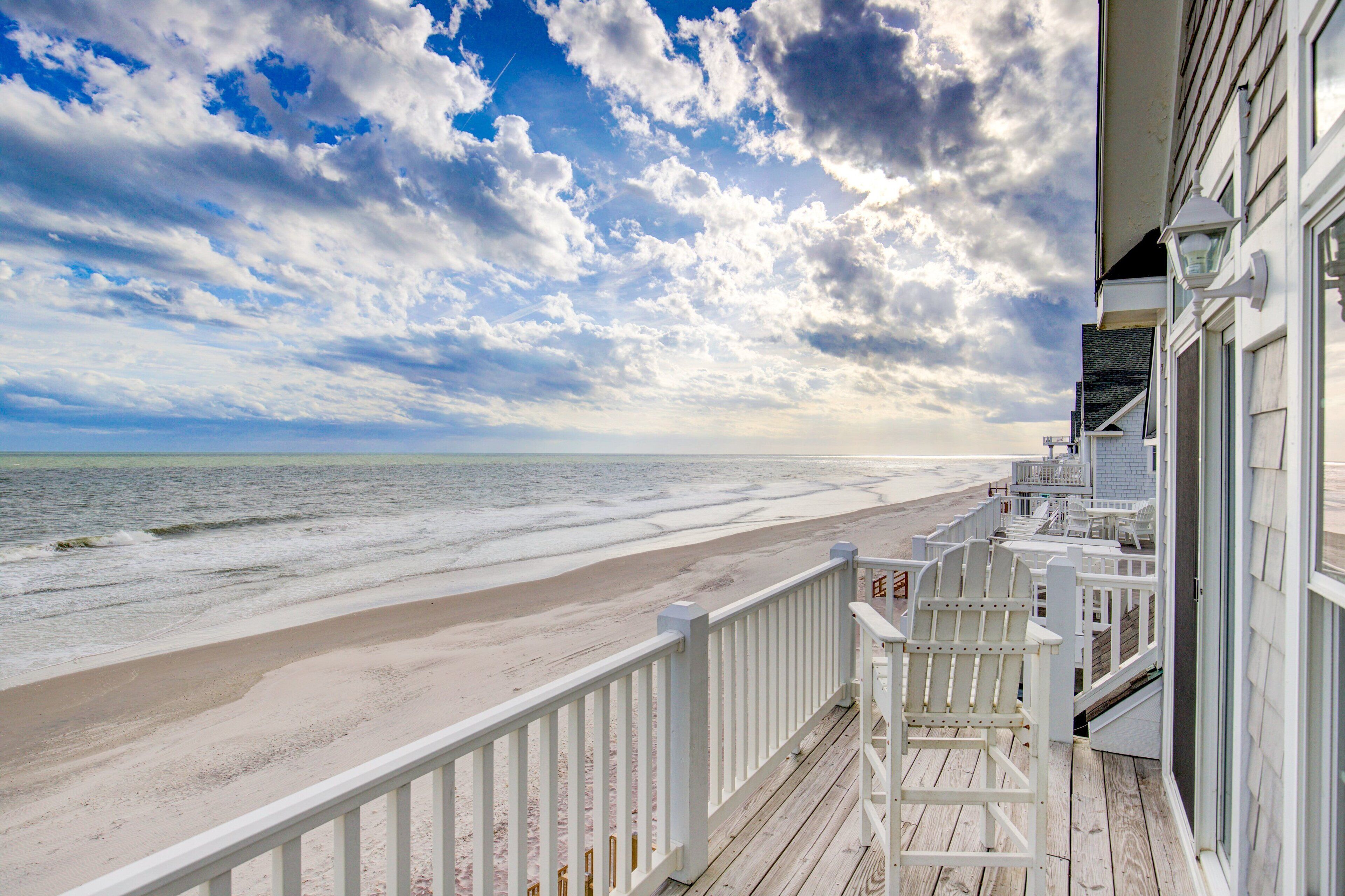 Une vue sur la plage depuis un balcon doté d’une terrasse en bois, de rampes blanches et d’une chaise Adirondack blanche.