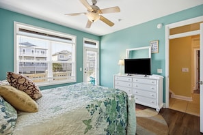 A bedroom with a bed, a ceiling fan, a TV, and a door leading to another room.