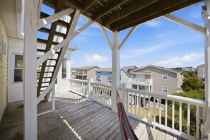 Um deck de madeira com corrimão branco, uma rede e vista para casas vizinhas.