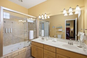 A modern bathroom with a large mirror, two sinks, a bathtub, and a glass-enclosed shower.