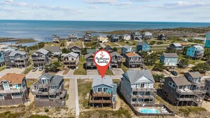 Uma área residencial costeira com várias casas de dois andares, uma piscina e vista para o oceano.