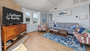 Uma sala de estar com televisão, sofá, poltrona listrada, mesa de centro e tapete estampado.