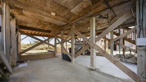 Estrutura de madeira aberta com piso de concreto, vigas visíveis e vista para o exterior.